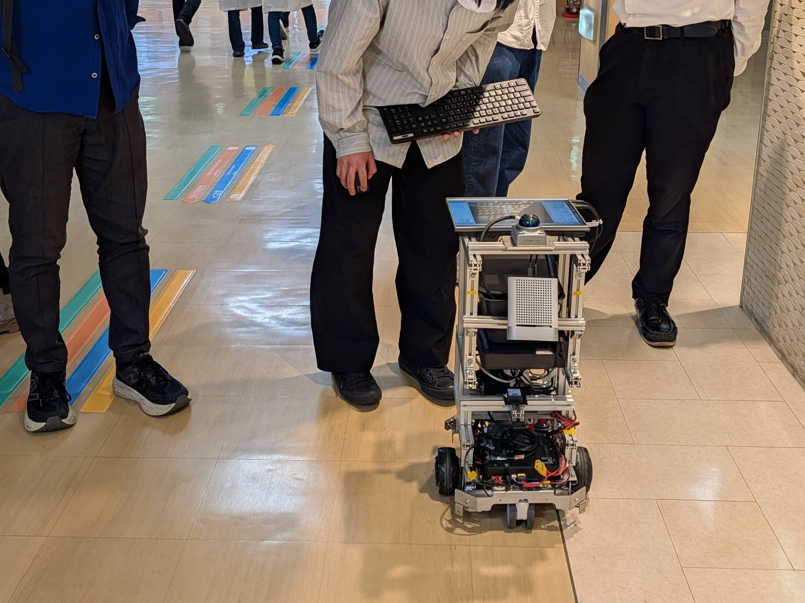 岡山大学病院の廊下を自律走行する実験用ロボットと、見守る研究者たち